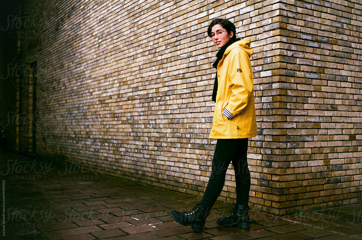 Model with a yellow raincaot walk next to a brick wall
