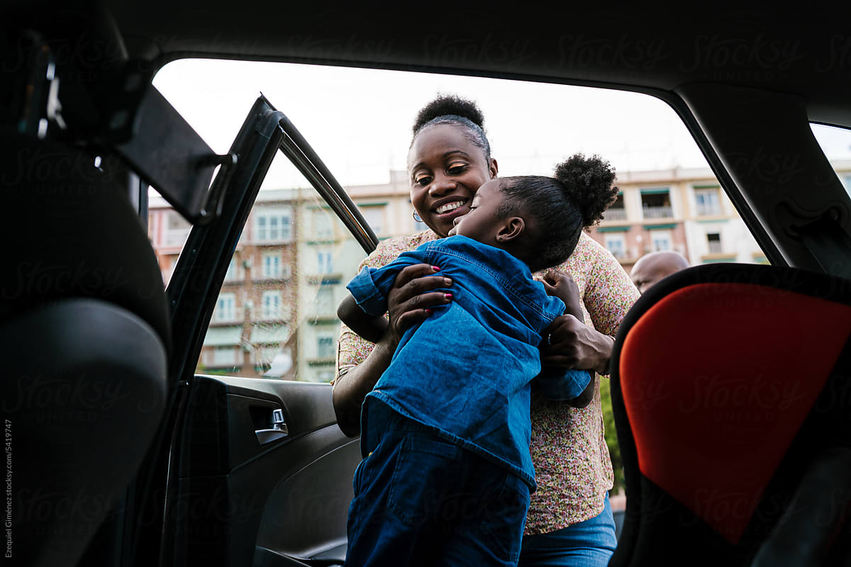 Happy mother placing daughter on back seat