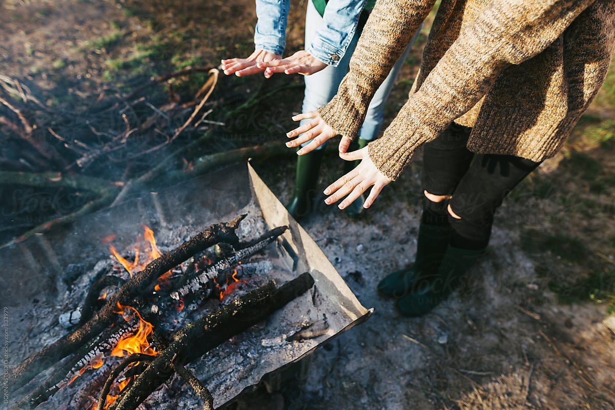 Overhead of hands of women warming over a bonfire.