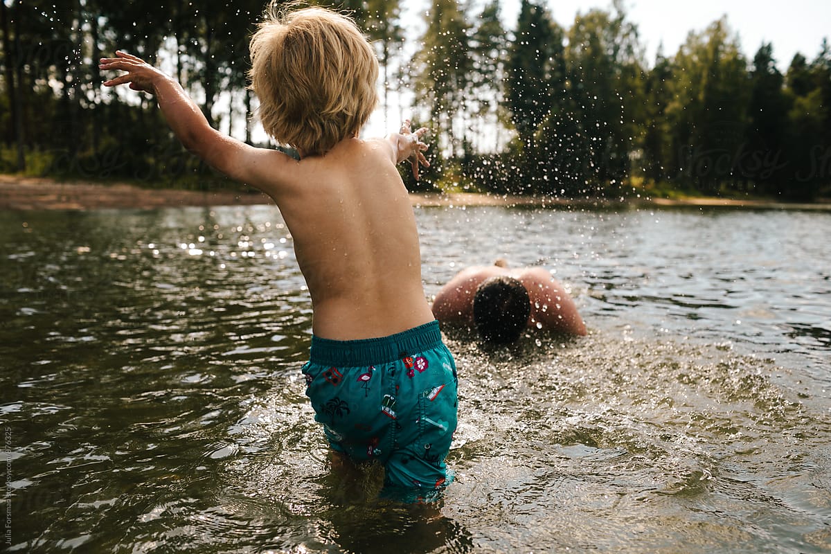 Little boy splashes water at his brother who is ducking in the water.
