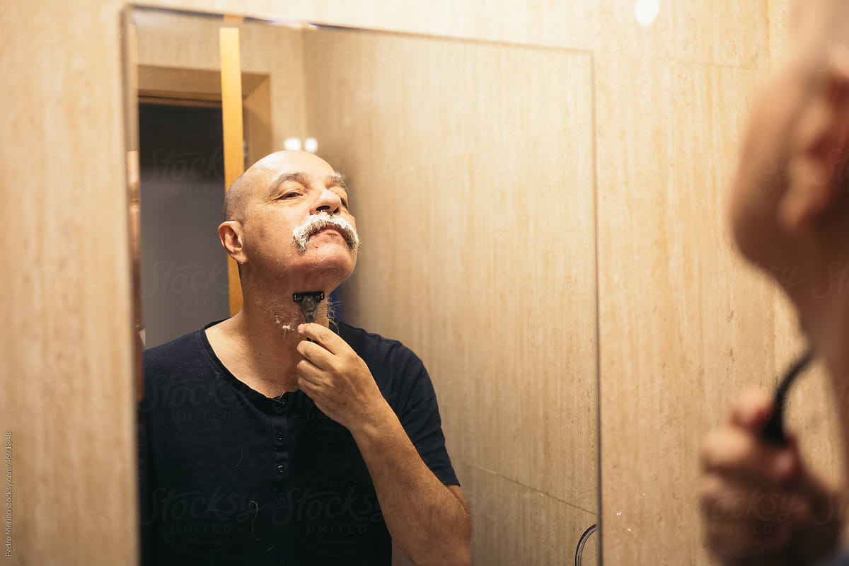 A man shaving his beard in front of the mirror