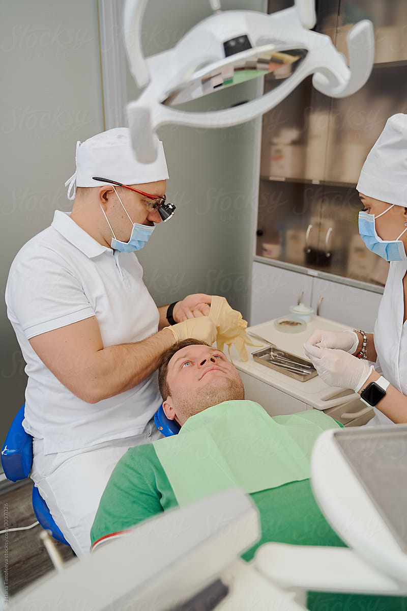 a dentist in a dental clinic puts on rubber gloves before looking at the client\'s teeth