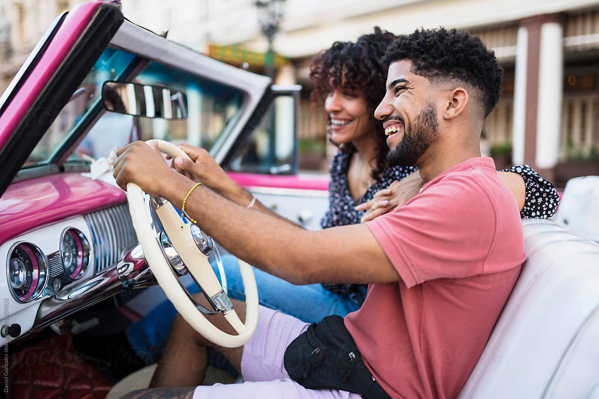 Cheerful Cuban couple driving in retro cabriolet car