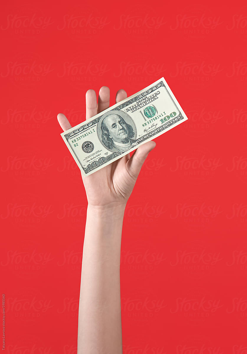 Female hand holding one hundred-dollar bill on bold red background.
