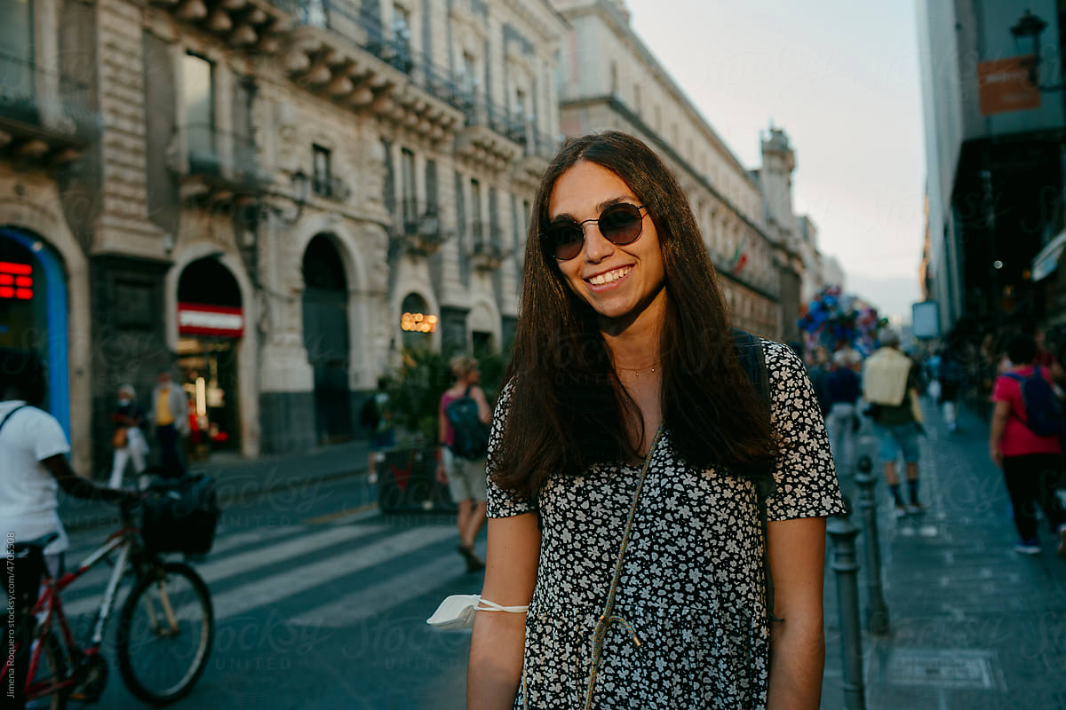 Attractive woman with sunglasses in sunlight in city street smiling.