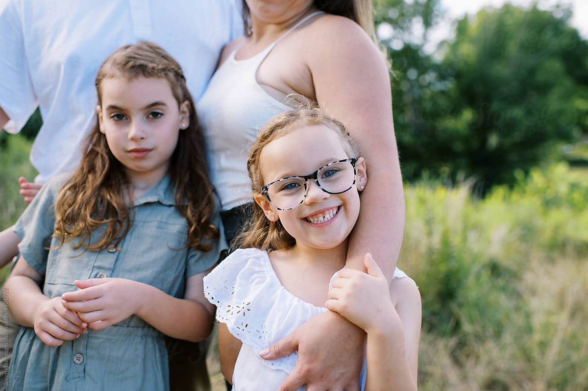 Little happy girl with glasses smiling while holding her mother\'s arm