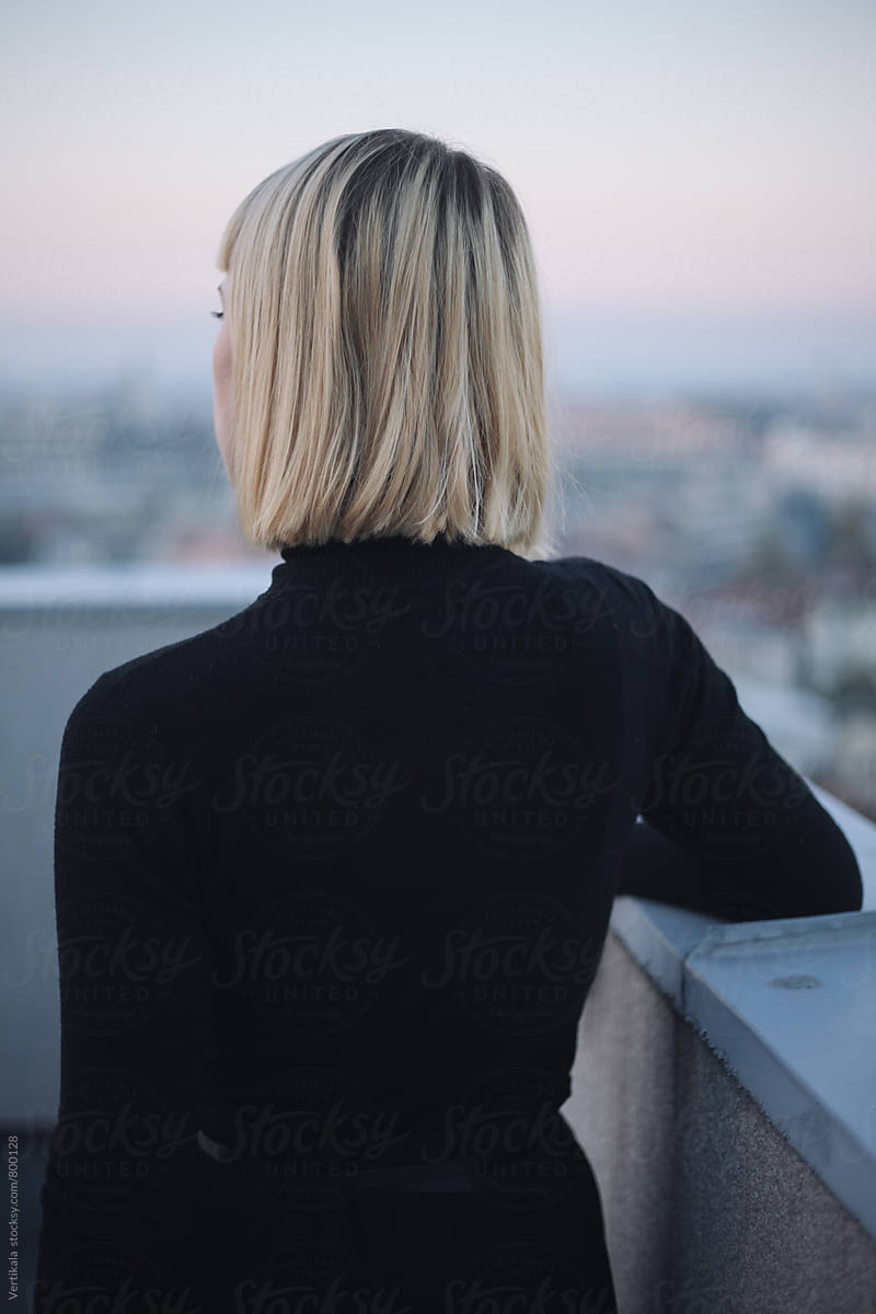 Blonde woman on the roof of the building during sunset from behind