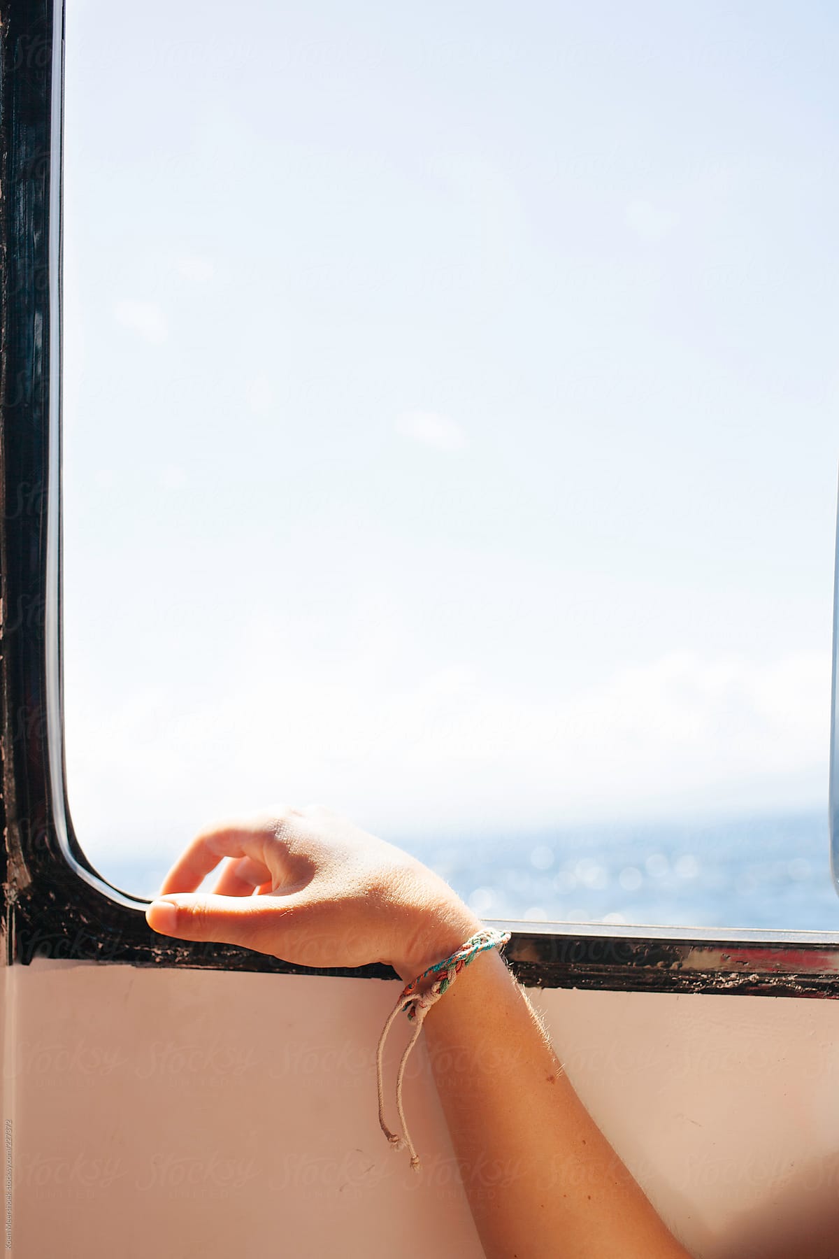Female hand with bracelets leaning on a window of a boat.