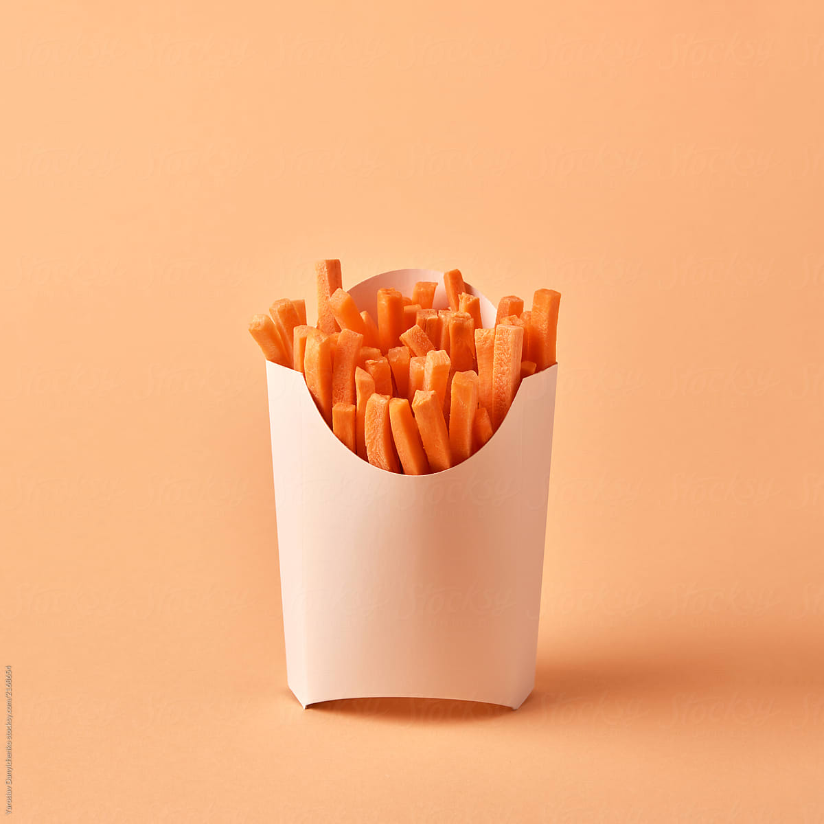 Natural fresh carrot sticks in a paper box on an orange paper ba