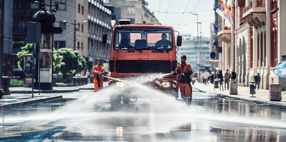 two street-sweeping workers using a  hose to clean off litter, street sweepe