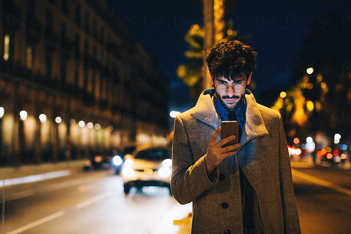 Portrait of a handsome businessman using a smartphone in the street at night.