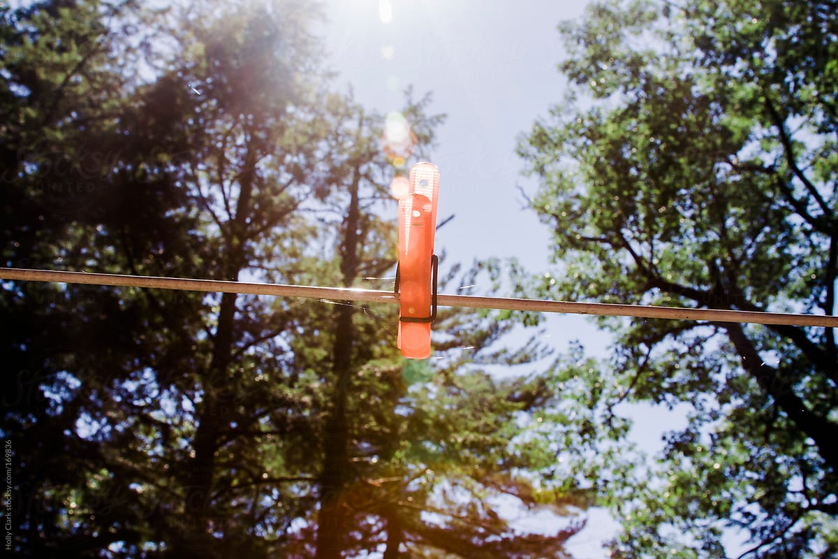 Summer sun shines down on an orange clothespin on a laundry line