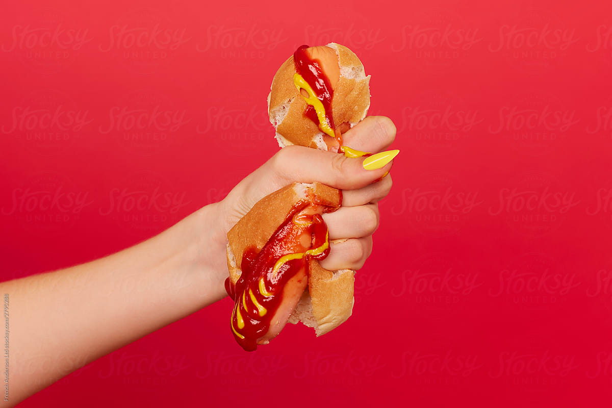 Woman\'s hand with painted nails squeezes hotdog