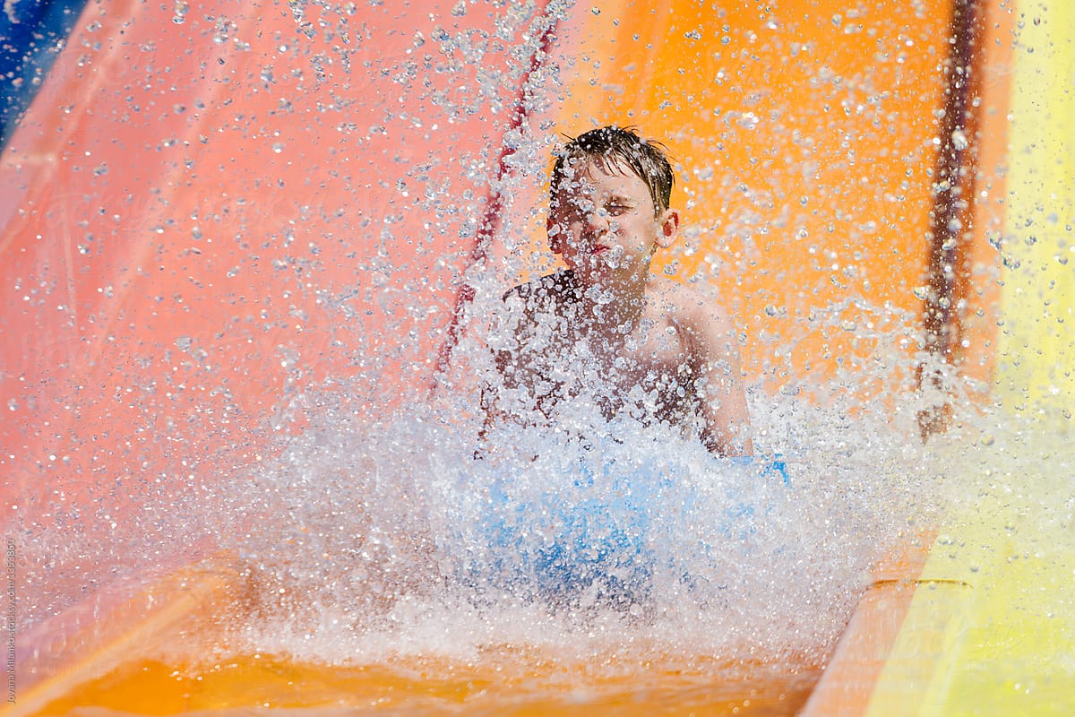 Young boy having a lot of fun sliding down the water tube in aqua park making a big splash