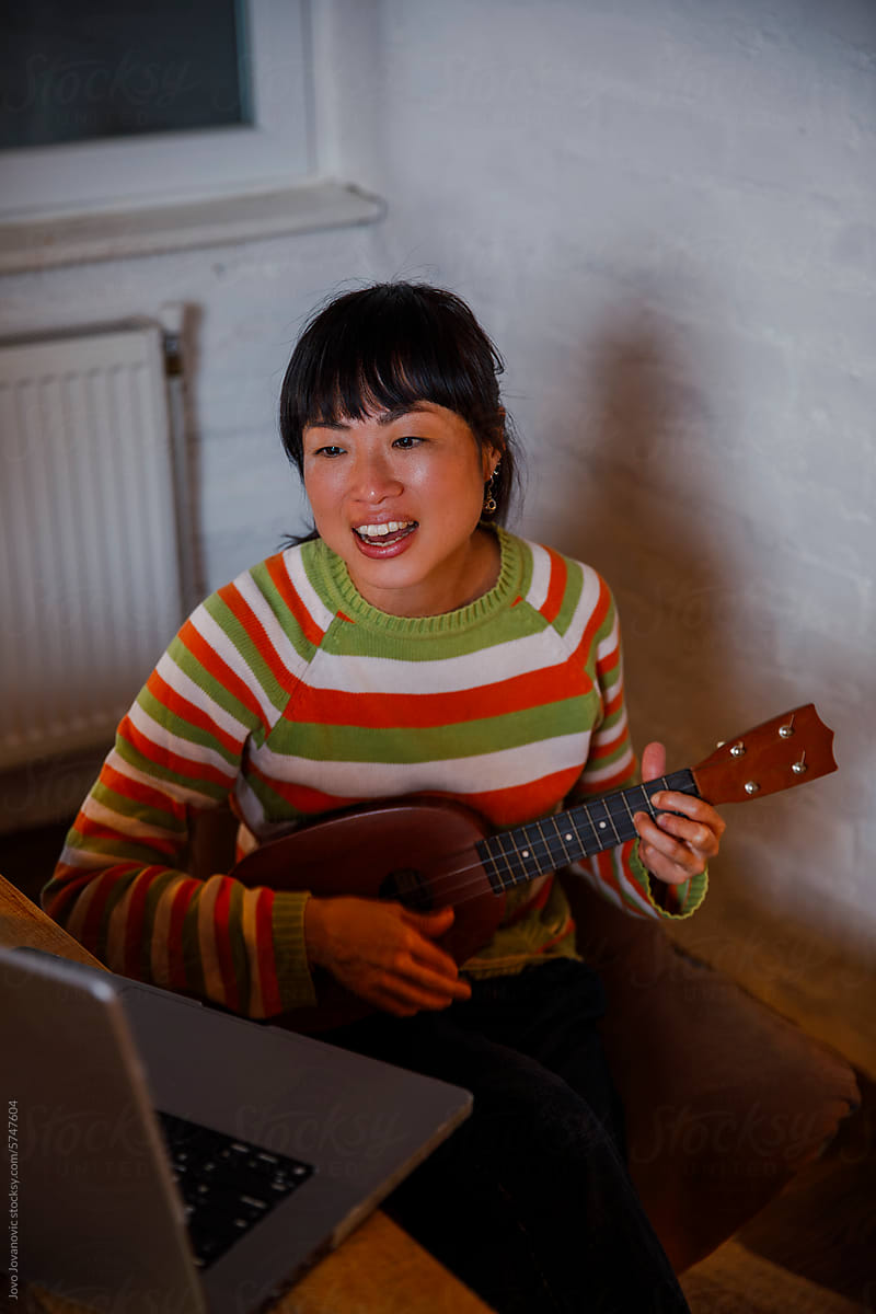 Woman learning playing ukulele through online session on laptop