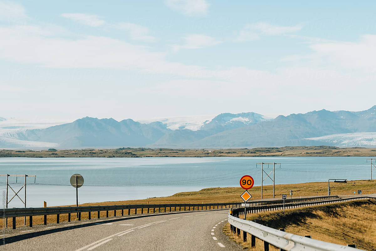 Open empty asphalt road through mountains, glacier, ocean on horizon