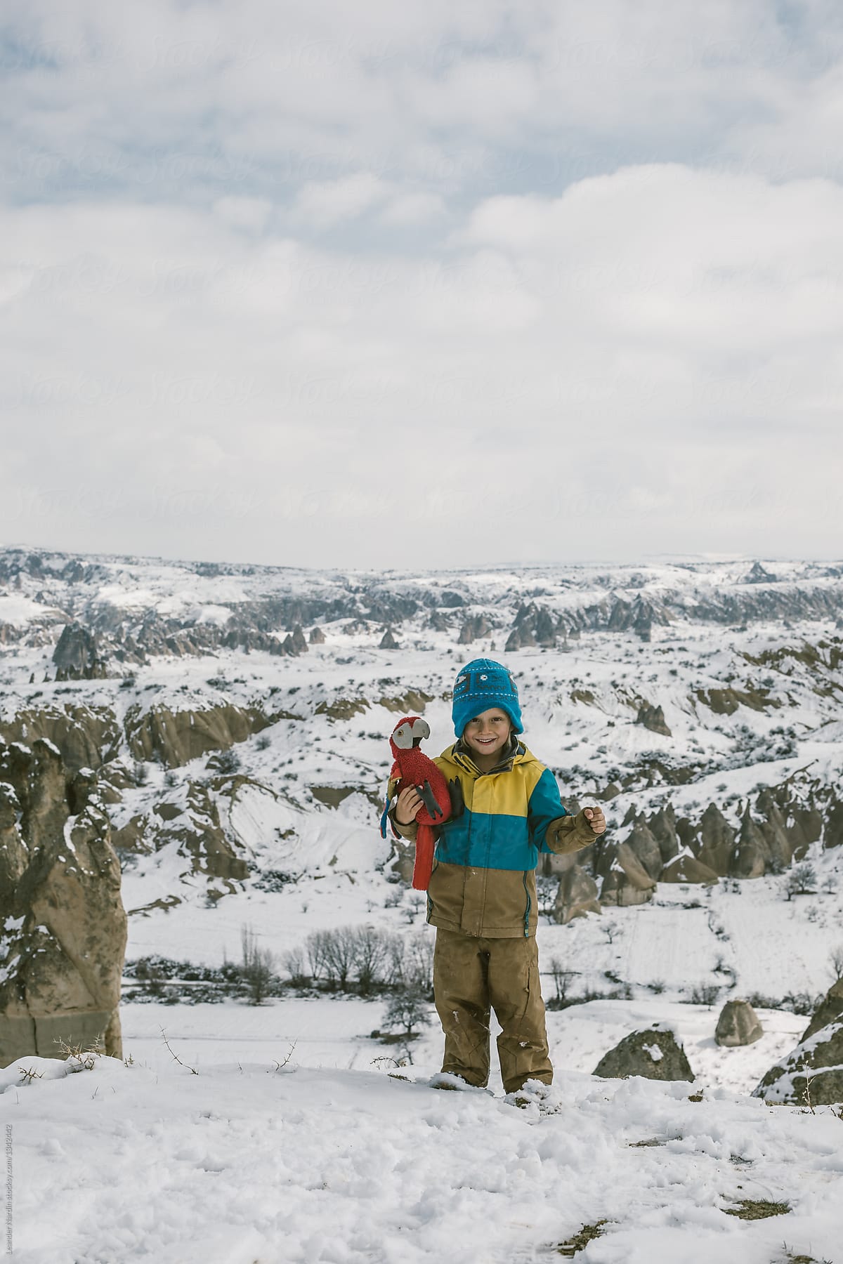smiling toddler holding his red parrot plushy toy in snowcovered landscape of cappadocia, turkey