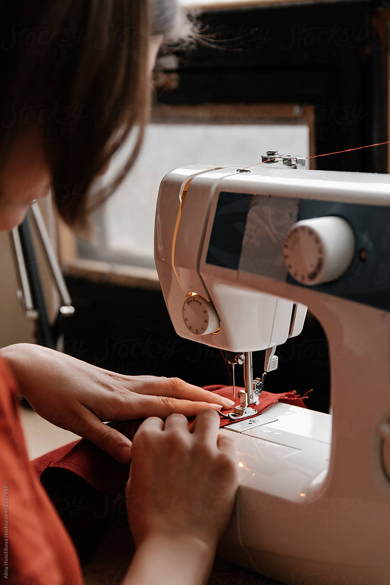 Dressmaker holding piece of red tissue on sew machine.