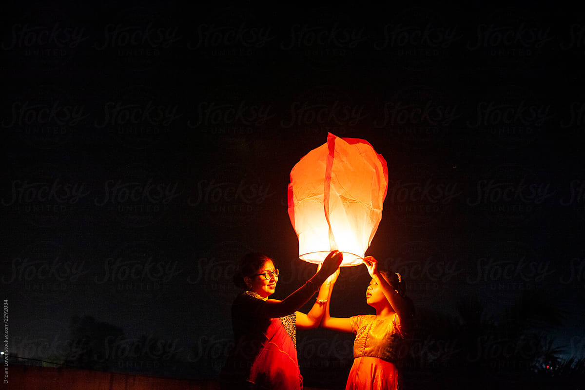 Little Girl And Her Mother holding Sky Lantern To The Sky At Twilight