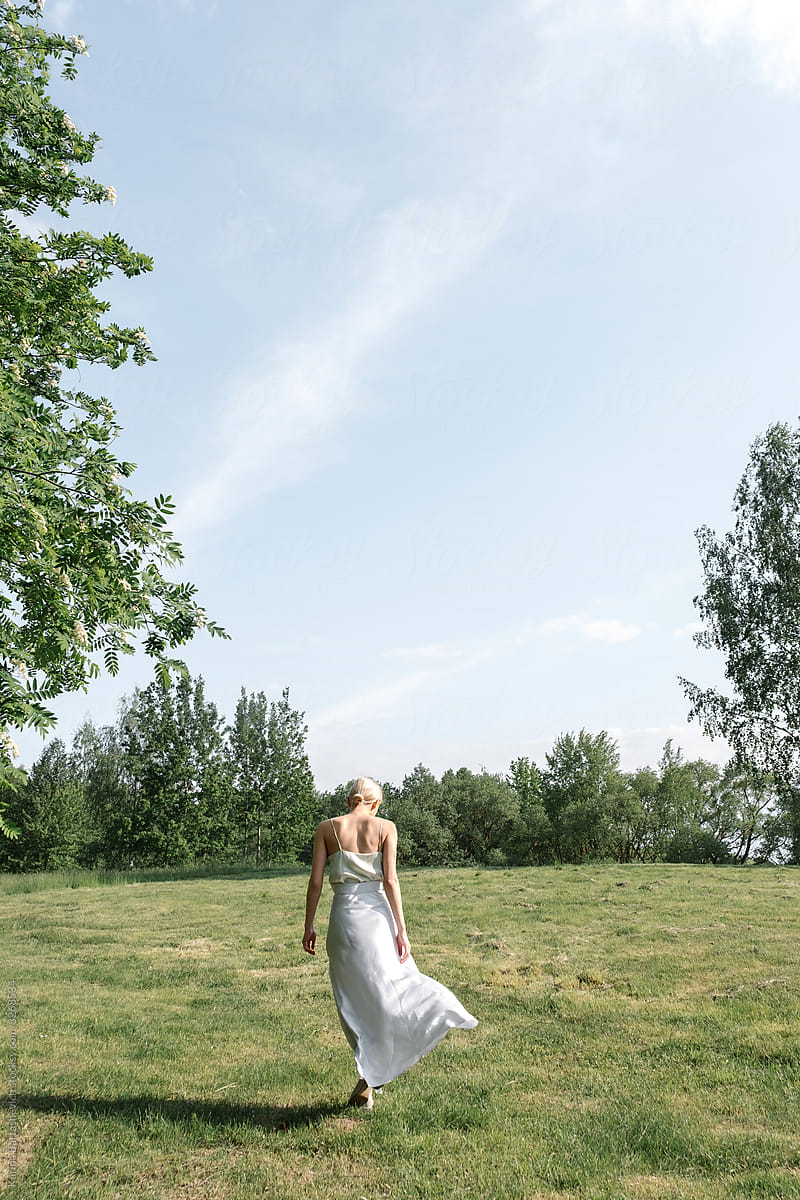 a girl with blond gathered hair in a white flying long dress that develops in the wind in nature near the lake