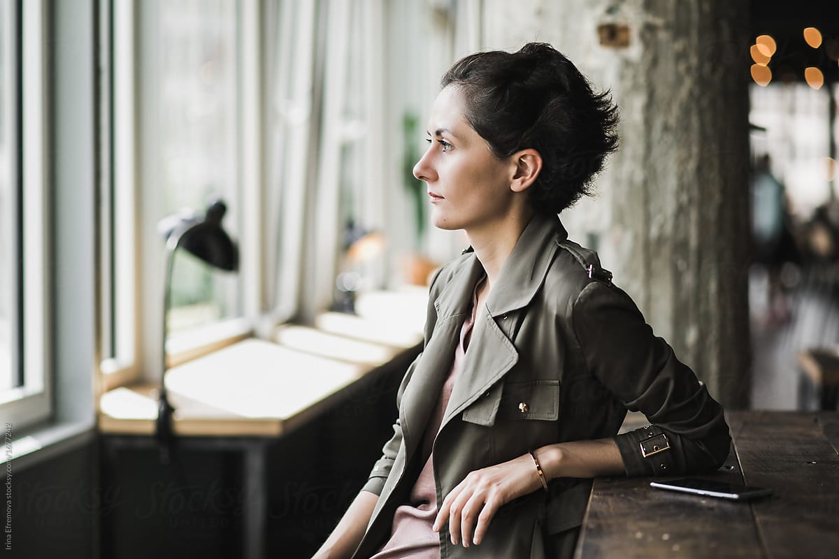 Short Dark Haired Woman Sitting In A Cafe Waiting By Stocksy