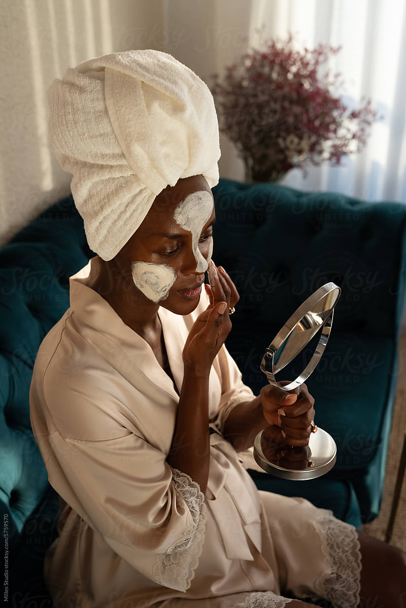 African American woman applying facial clay mask for cleansing