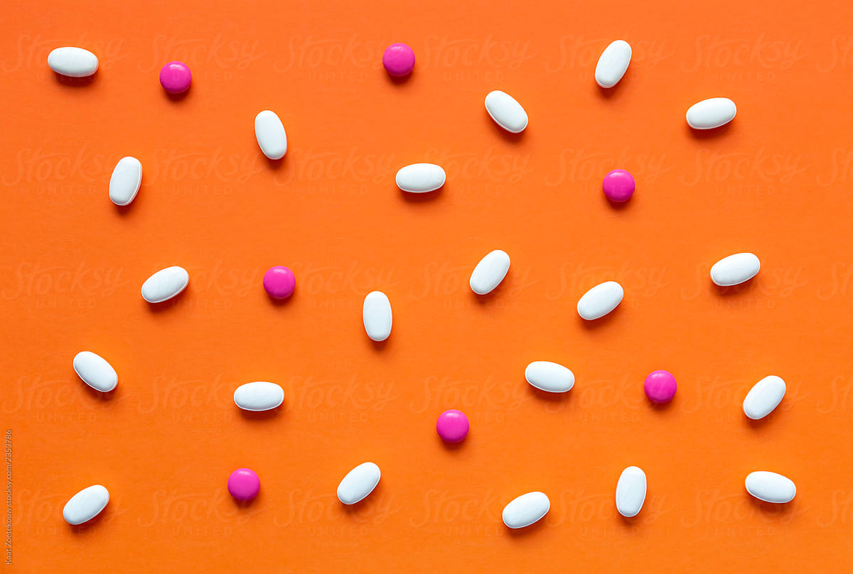 Various pink and white pills on a bright orange background