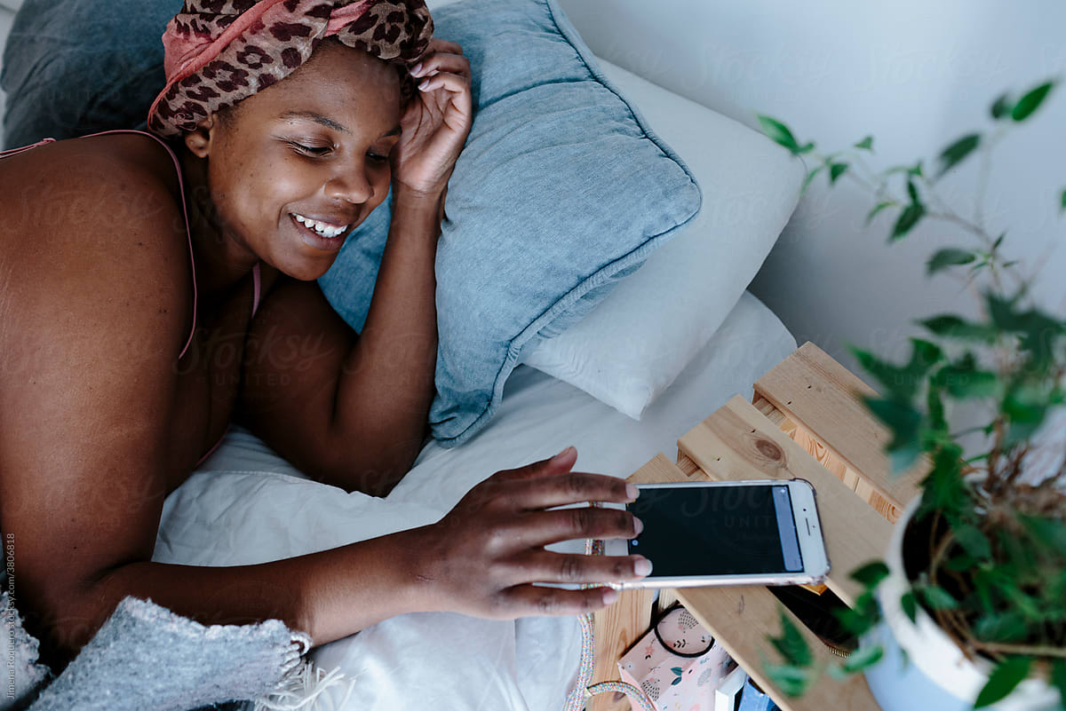 Woman in bed turning off alarm on cell phone smiling