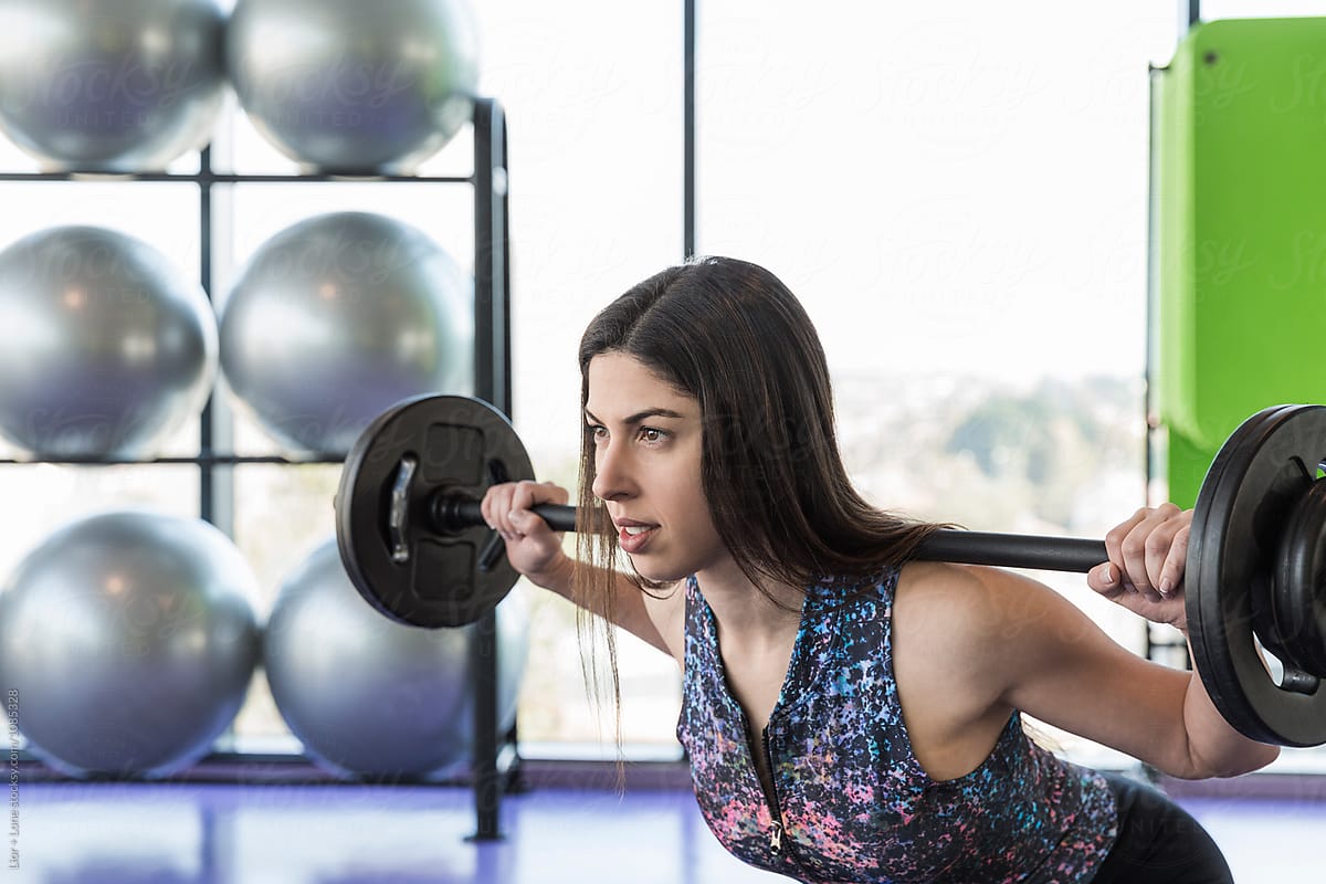 Closeup of female athlete exercising with barbell in a studio