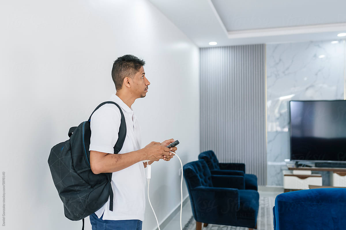 Positive slim man with bagpack and smartphone in light living room
