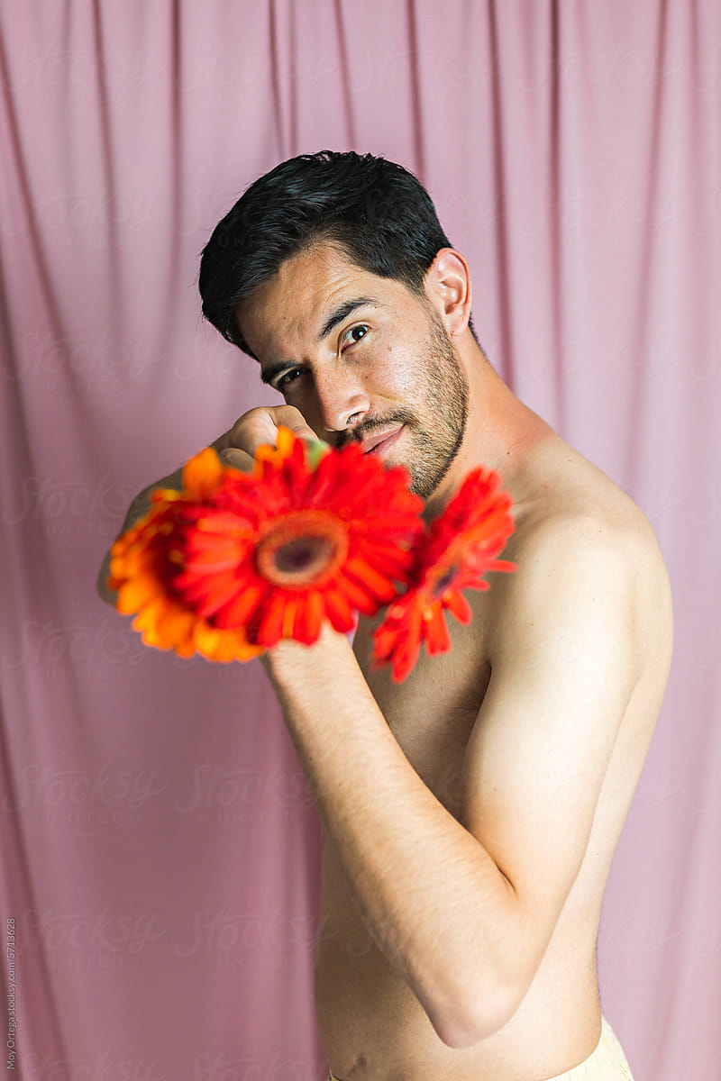 Bare man holding a bouquet of gerbera flowers pointed at the camera