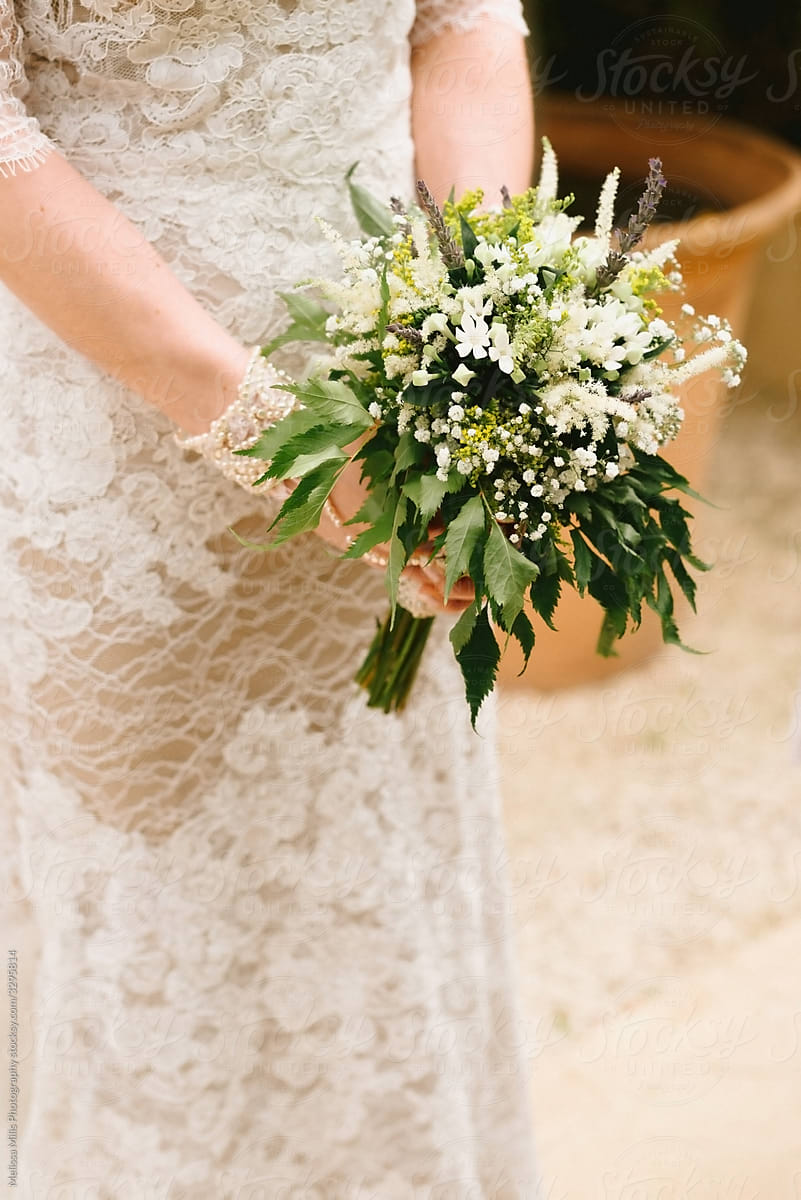 Bride with vintage wedding dress holding a white and green wedding bouquet in her hands