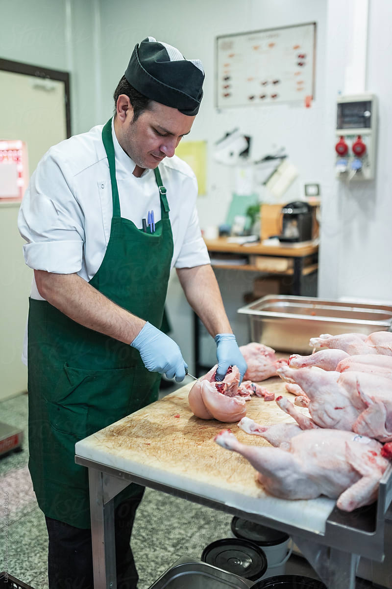 man cutting chicken meat in the back of a butcher shop