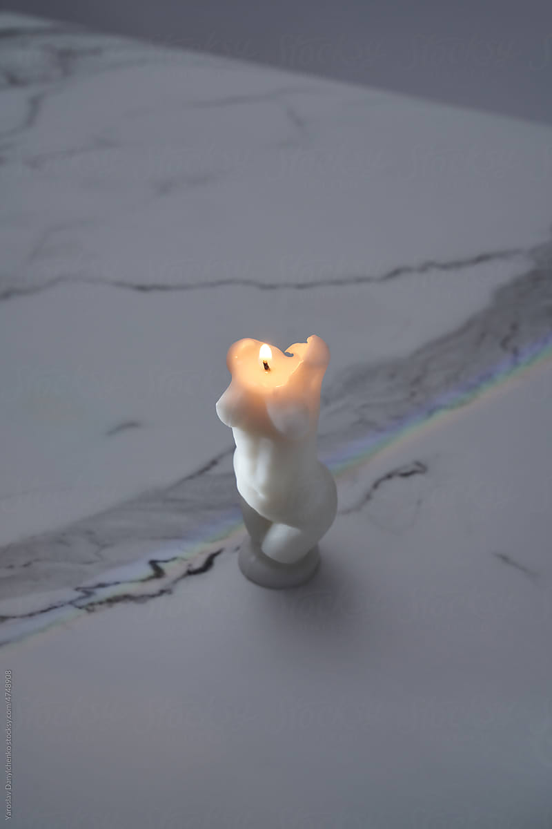 Candle with female shape on marble background.