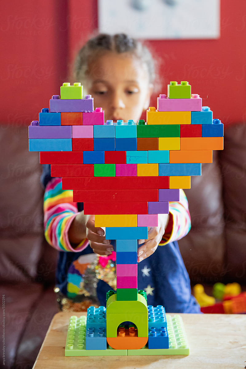 Child building a heart shaped structure with vibrant lego blocks