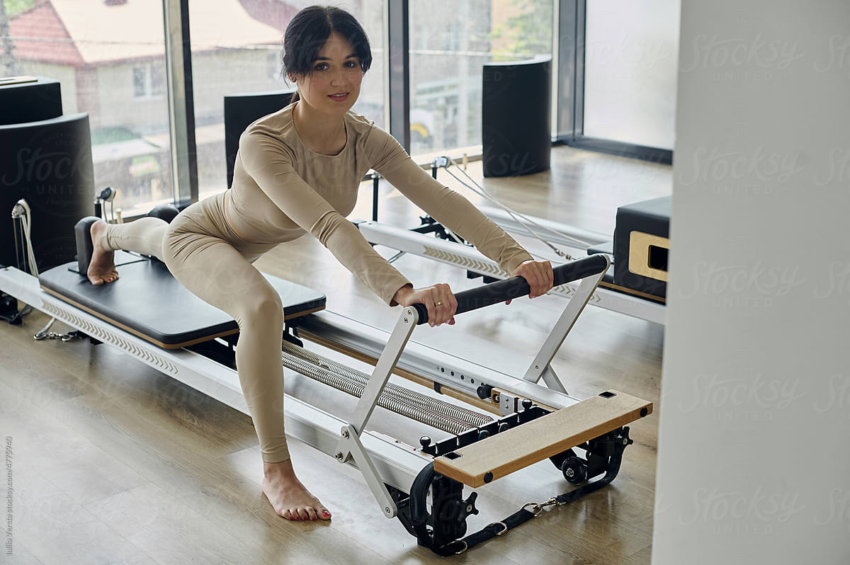 Woman training pilates on the reformer bed. - Stock Photo