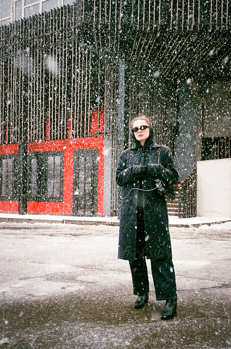 Girl in sun glasses stand in an empty street during a snowstorm