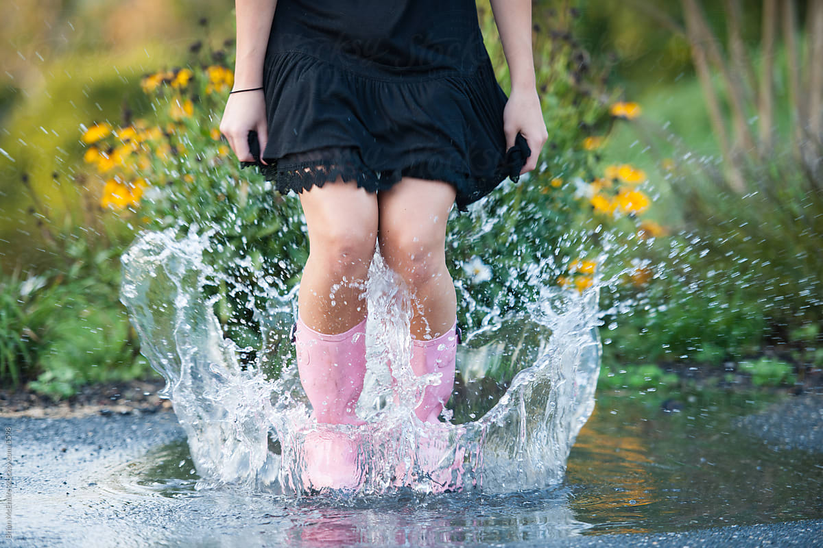 Woman with pink rain boots splashes in a puddle