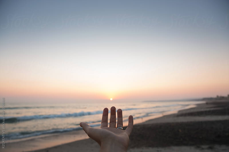 Hand reaching out to the sun at sunset.