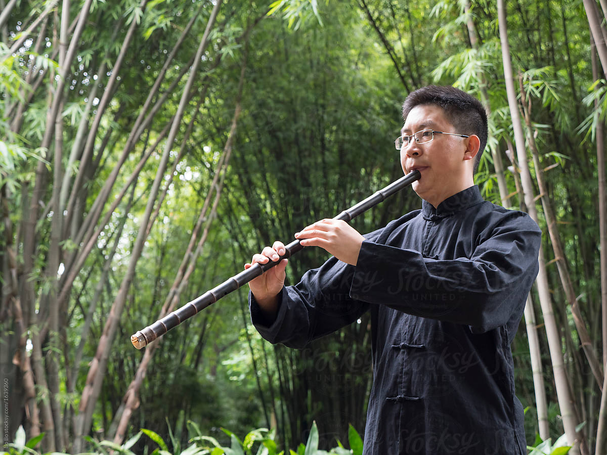 One Chinese man playing vertical bamboo flute in the bamboo wood