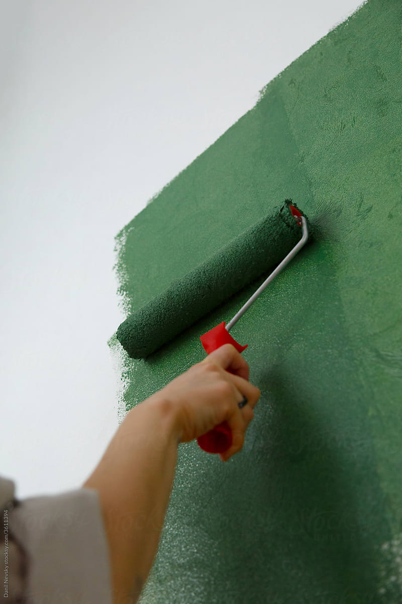 Crop woman painting wall at home