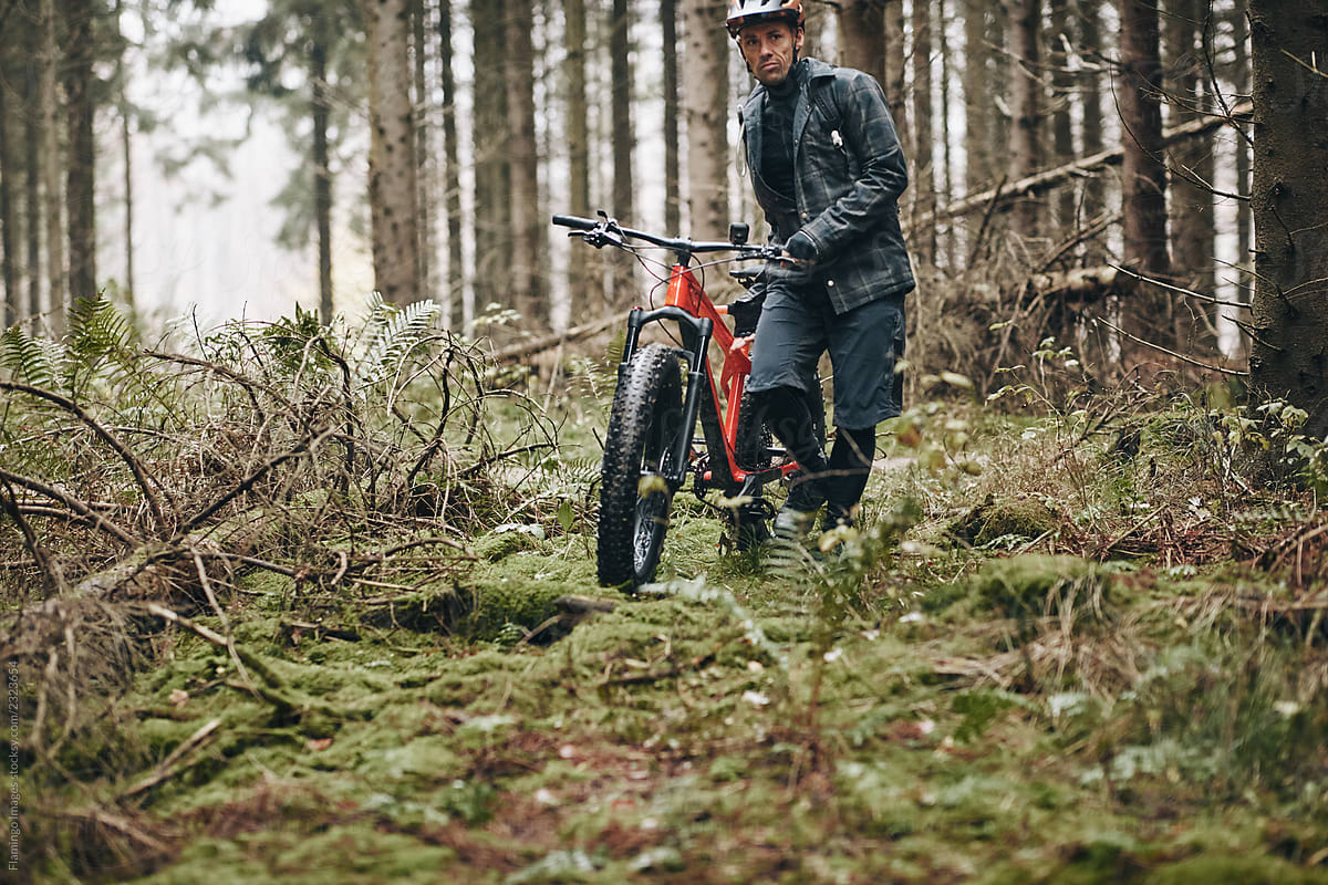 Man pushing his mountain bike along a dense forest trail
