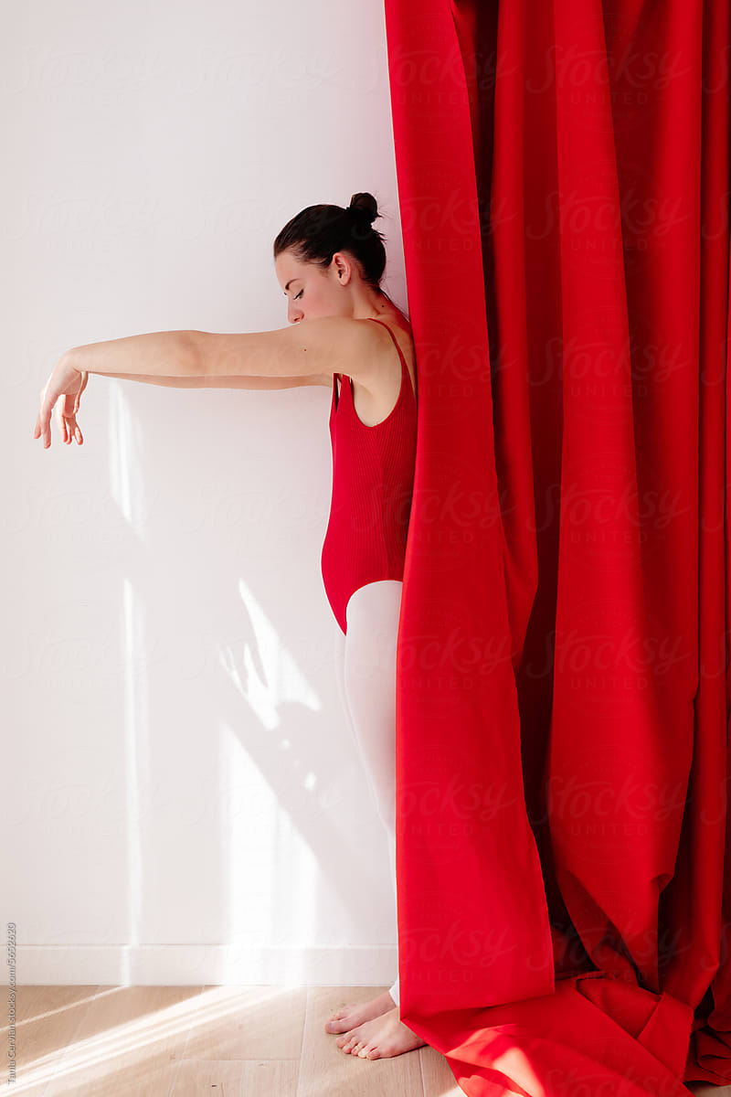 Slim young woman standing in dance pose at red curtain
