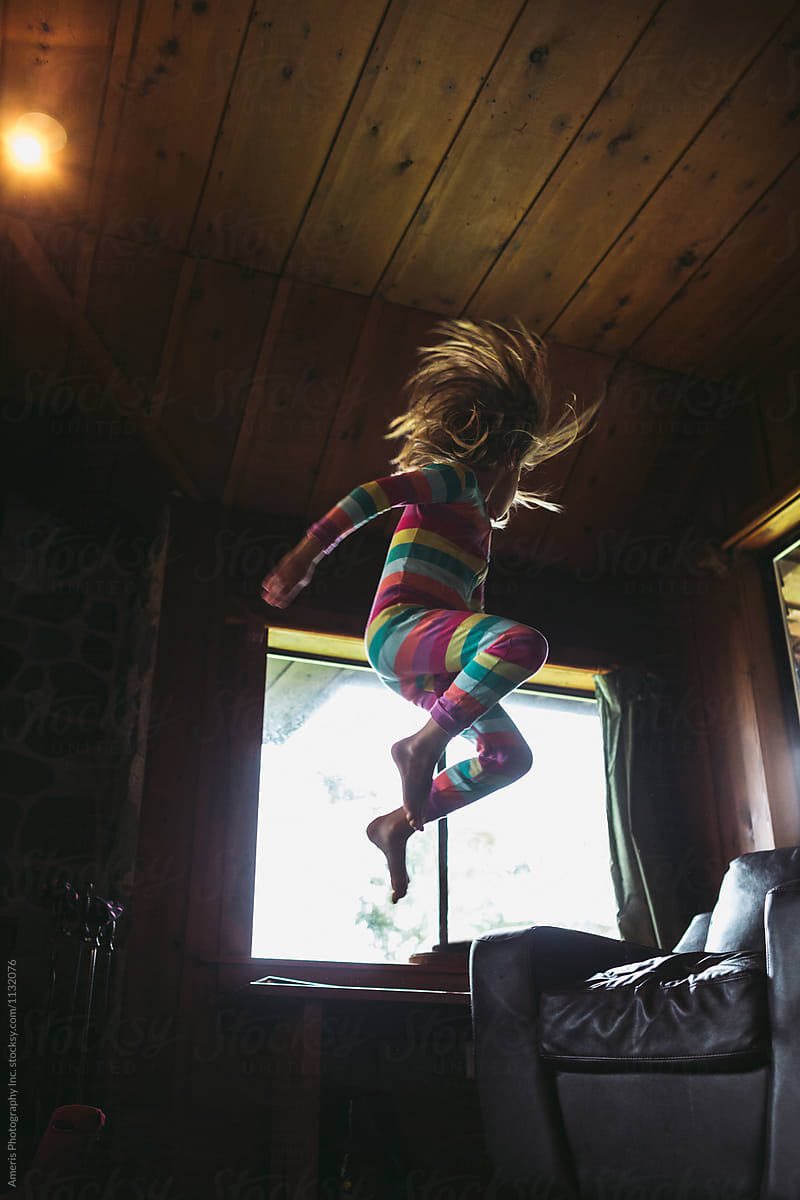 Young caucasian girl jumping off couch inside wearing pj\'s