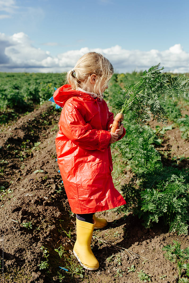 Anonymous child in raincoat and rubber boots with carrots