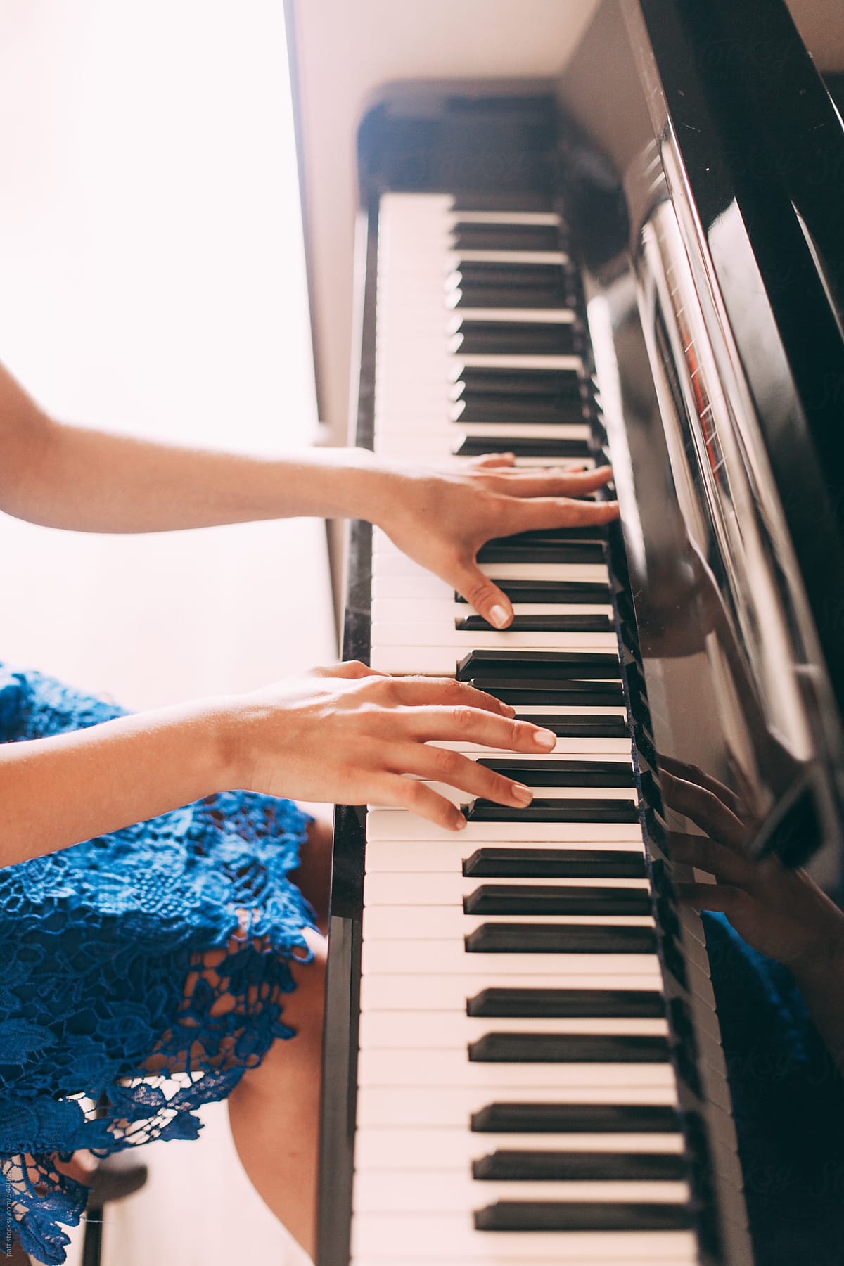 Hands of a sitting girl in blue dress playing the piano