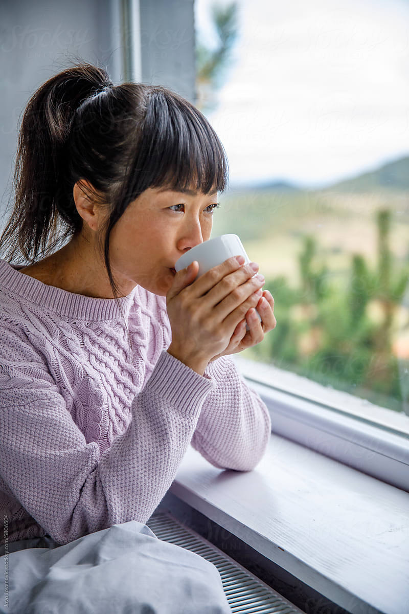 Woman drinking coffee while looking through window at home
