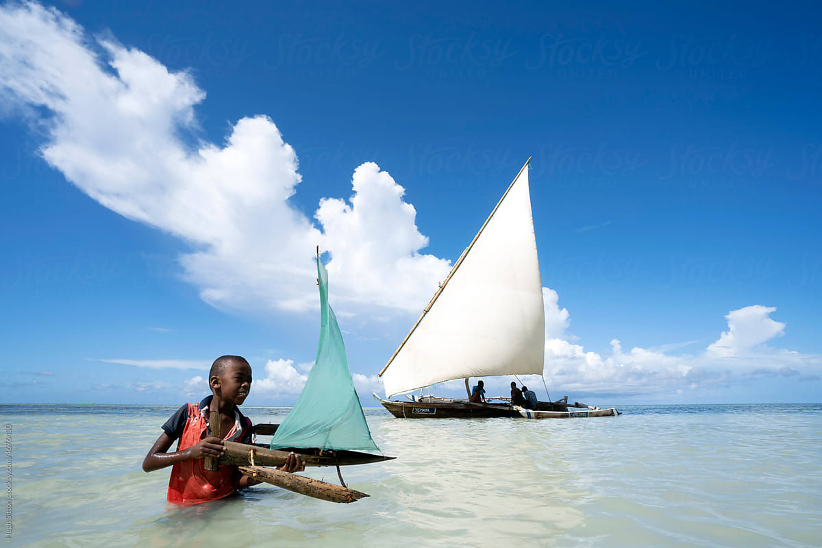 Boy playing with toy boat, traditional dhow in the background.