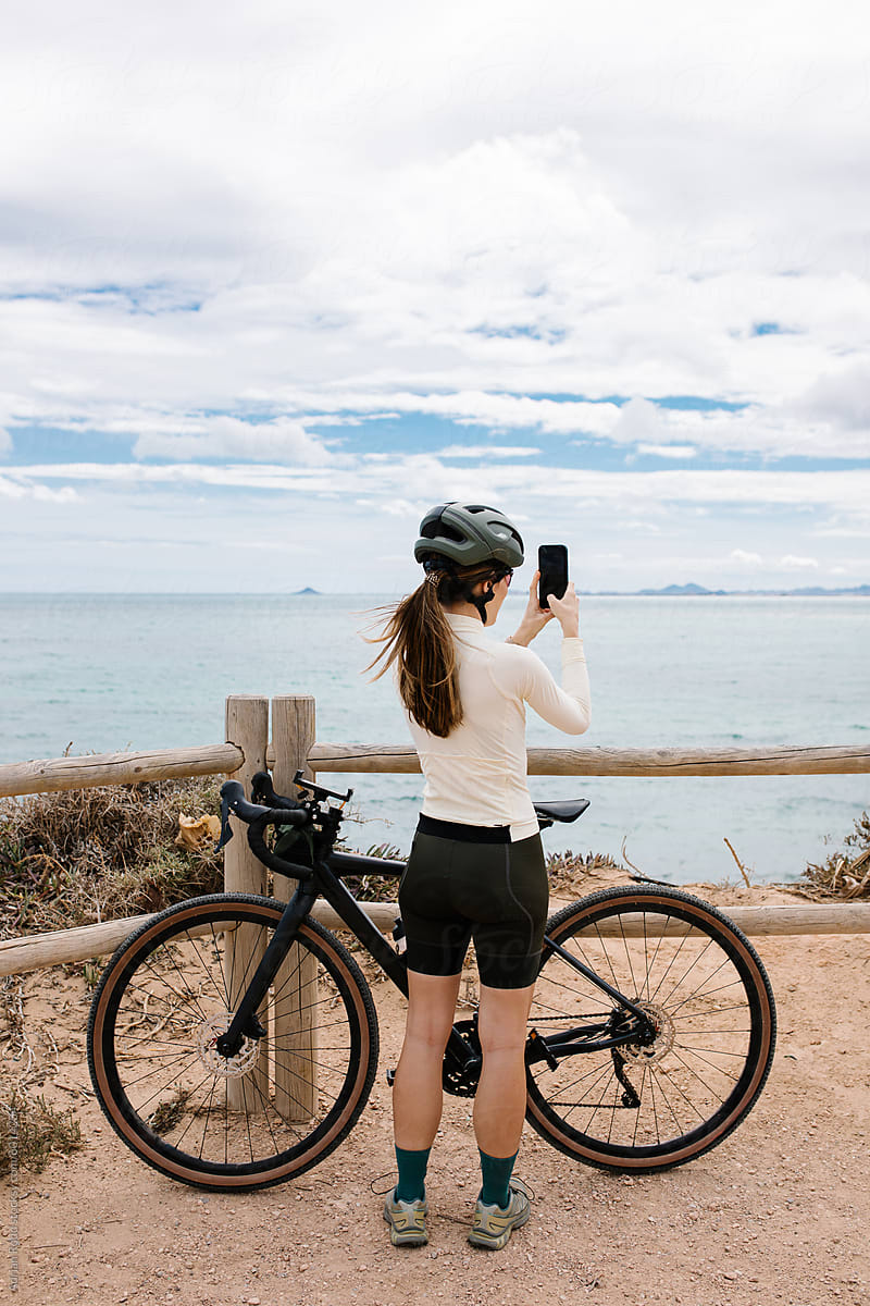 A cyclist uses a smartphone to take a picture of the seascape