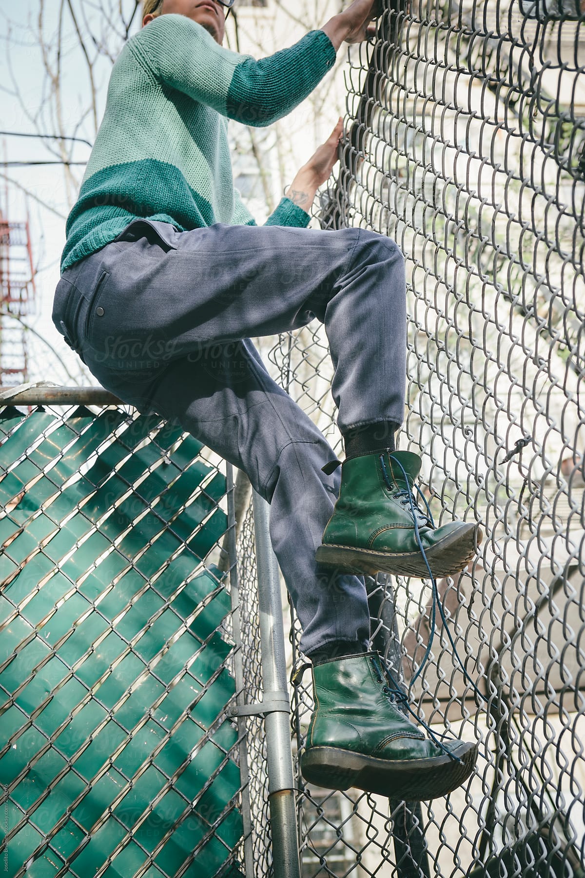 Stylish Young Man with Bleached Blond Hair in Spring and Summer Fashion Climbing a Fence